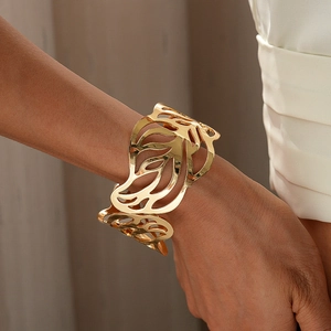 Macro shot of gold wide open cuff bracelet featuring intricate hollow leaf patterns