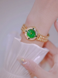 Close-up of women gold watch with green dial and crystals on white ruffled sleeve cuff