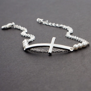 Elegant multi-layer silver cross bracelet with white freshwater pearls on dark background