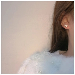 Close-up model shot of gold bow stud earrings with a white pearl on the earlobe