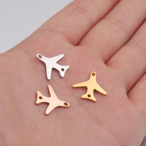 Close-up of three airplane-shaped pendants in silver, gold, and rose gold on a palm