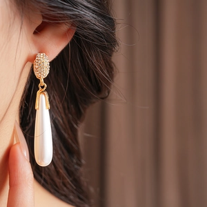 Close-up of gold drop earrings with sparkling rhinestones and white teardrop pearls on model