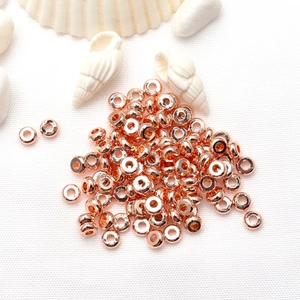 Rose gold flat round spacer beads for DIY jewelry making on white textured background