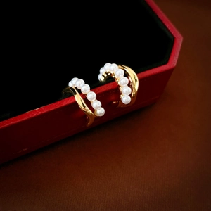 Detailed macro shot of C-shaped gold pearl earrings resting on a luxury red jewelry box