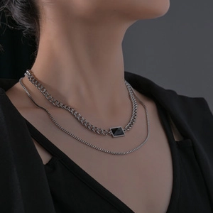 Close-up of minimalist layered silver necklaces with black rectangular pendant on male model