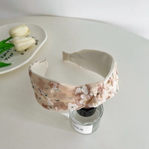 Close-up of beige mesh floral headband with knotted design on a glass bottle display