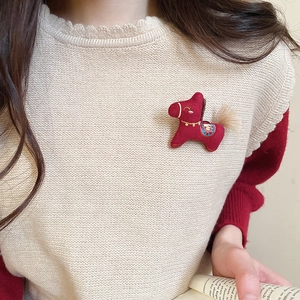 Detail of a handmade red fabric pony brooch with embroidery pinned on a beige vest