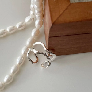 Detailed view of silver hollow wave ring displayed with pearls on a wooden frame