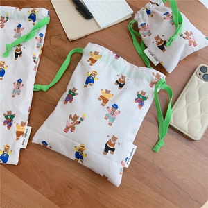 Flat lay of a bear-printed cotton drawstring storage bag on a wooden table with stationery