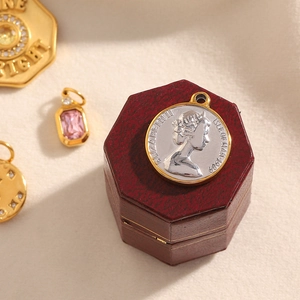 Detail of Elizabeth II coin pendant with gold frame and pink gemstone on a red jewelry box