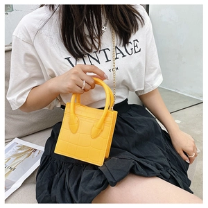 Macro view of yellow crocodile texture crossbody bag with gold chain strap detail