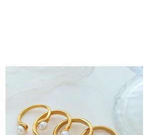 Close-up of four elegant gold open rings featuring white pearls on white lace fabric