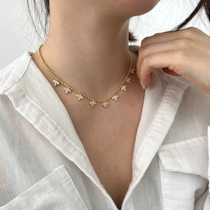 Detail of gold beaded necklace with nine white zircon leaf pendants on model wearing white