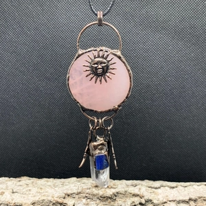 Close-up of vintage sun god pendant with rose quartz and hanging crystal on wood