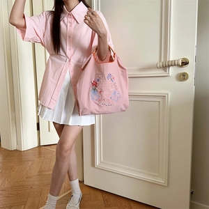 Vue détaillée d'un sac cabas en toile rose avec broderie florale tenu par un mannequin