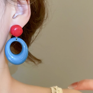 Gros plan de boucles d'oreilles en résine contrastée rouge et bleue sur l'oreille