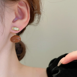 Close-up of golden and caramel oval drop earrings worn by a model for a vintage look