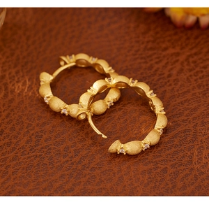 Close-up of golden brushed earrings with white zircon on brown leather texture