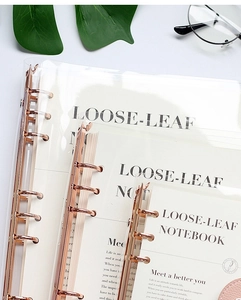 Detailed view of stacked transparent PVC notebook binders featuring stylish rose gold 6-ring clips