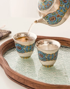 Close-up of tea pouring into a silver cloisonne cup with vibrant floral enamel details