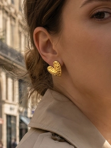 Detail of a vintage golden heart stud earring with hammered texture on a model