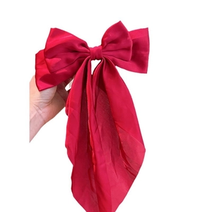 Elegant large red satin bow hair clip with long streamers held against a white background