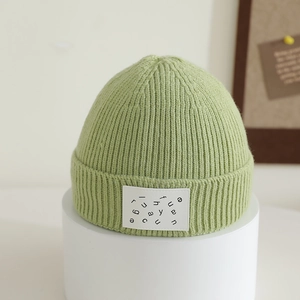 Detail of avocado green knit beanie with ribbed texture and white rectangular letter patch