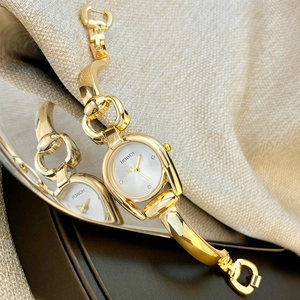Macro detail of gold horseshoe case watch with smooth metal link bracelet on white dial