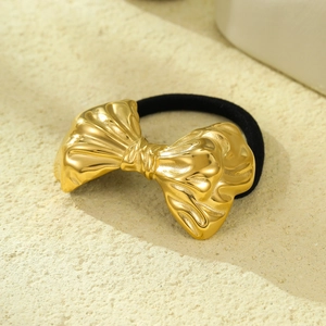 Close-up of golden bow-shaped metal hair tie with black elastic band on textured surface