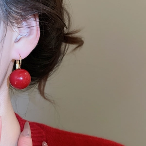 Close-up of a large glossy red resin bead earring with a gold plated clasp on model