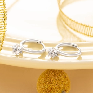 Minimalist silver huggie earrings with a single round zircon stone on a warm elegant backdrop