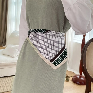 Close-up of geometric silk scarf styled as a belt on a model's green knit dress