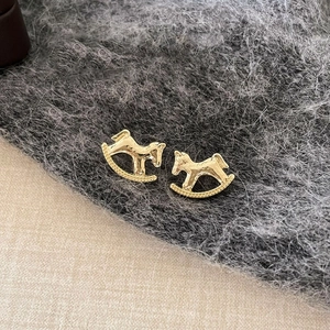 Detail of 18k gold plated rocking horse earrings with hammered metal texture on fabric
