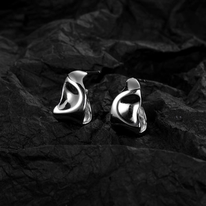 Artistic close-up of silver irregular geometric earrings on textured black paper