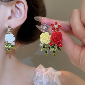 Close-up of floral crystal earrings with red and yellow resin petals and green leaves