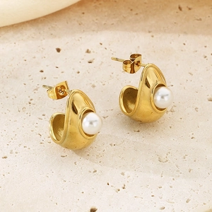 Detail shot of gold geometric earrings with pearls on a textured stone background