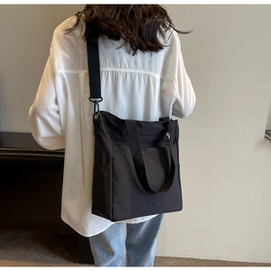 Detail view of a black nylon tote bag with adjustable shoulder strap on a model back