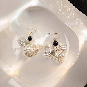 Elegant petal-shaped earrings with white resin pearls and black beads in a white dish