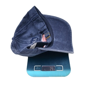 Navy blue cotton baseball cap with USA embroidery on a scale showing 74g weight