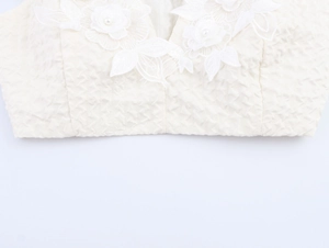 Détail d'un caraco blanc texturé avec des fleurs en dentelle 3D et des perles