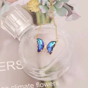 Detailed close-up of a gradient blue crystal butterfly pendant on a gold necklace chain