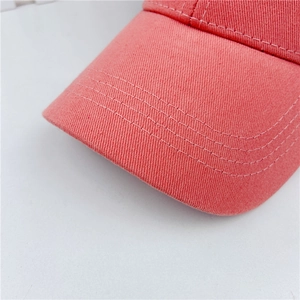Detailed close-up of parallel stitching on the cotton twill brim of a coral pink baseball cap