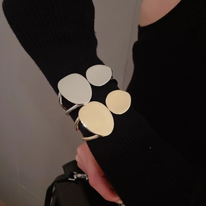 Irregular oval layered metal cuffs in gold and silver finish on a black knit sleeve