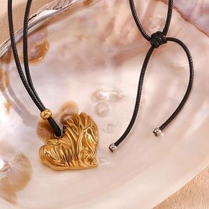Detail of gold wrinkled heart pendant on a black cord over a pearlescent shell background