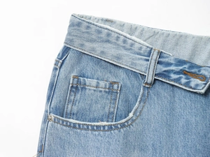 Dettaglio dei jeans in denim azzurro con vita ripiegata, passanti e taschino per monete