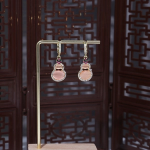 Detail of gold gourd earrings with pink cat eye stone and white zircon inlays