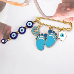 Detail of gold evil eye safety pin with blue cross and hand charms for clothing decor