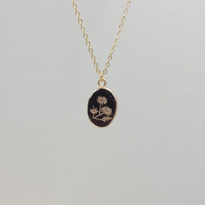 Detailed view of oval black pendant with gold floral engraving on stainless steel chain
