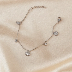 Elegantes Edelstahl-Muschelarmband mit funkelnden Strasssteinen auf goldenem Seidenstoff