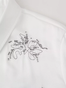 Detailed macro shot of dark grey bead embroidery on white woven fabric of a shirt